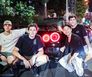 Un grupo agachado junto a las luces traseras de un deportivo japonés, de noche