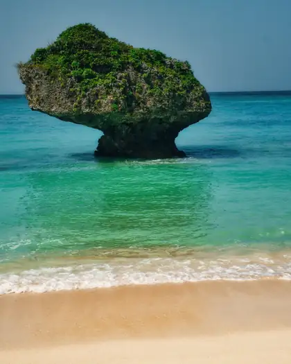 Una roca con vegetación en una playa de agua turquesa de Okinawa