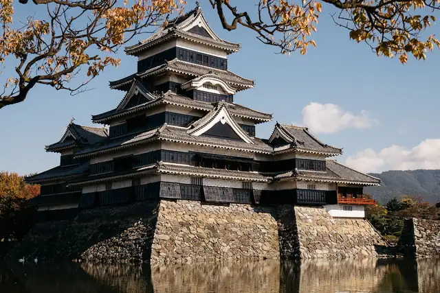 El castillo de Matsumoto entre ramas de otoño, reflejado en el foso