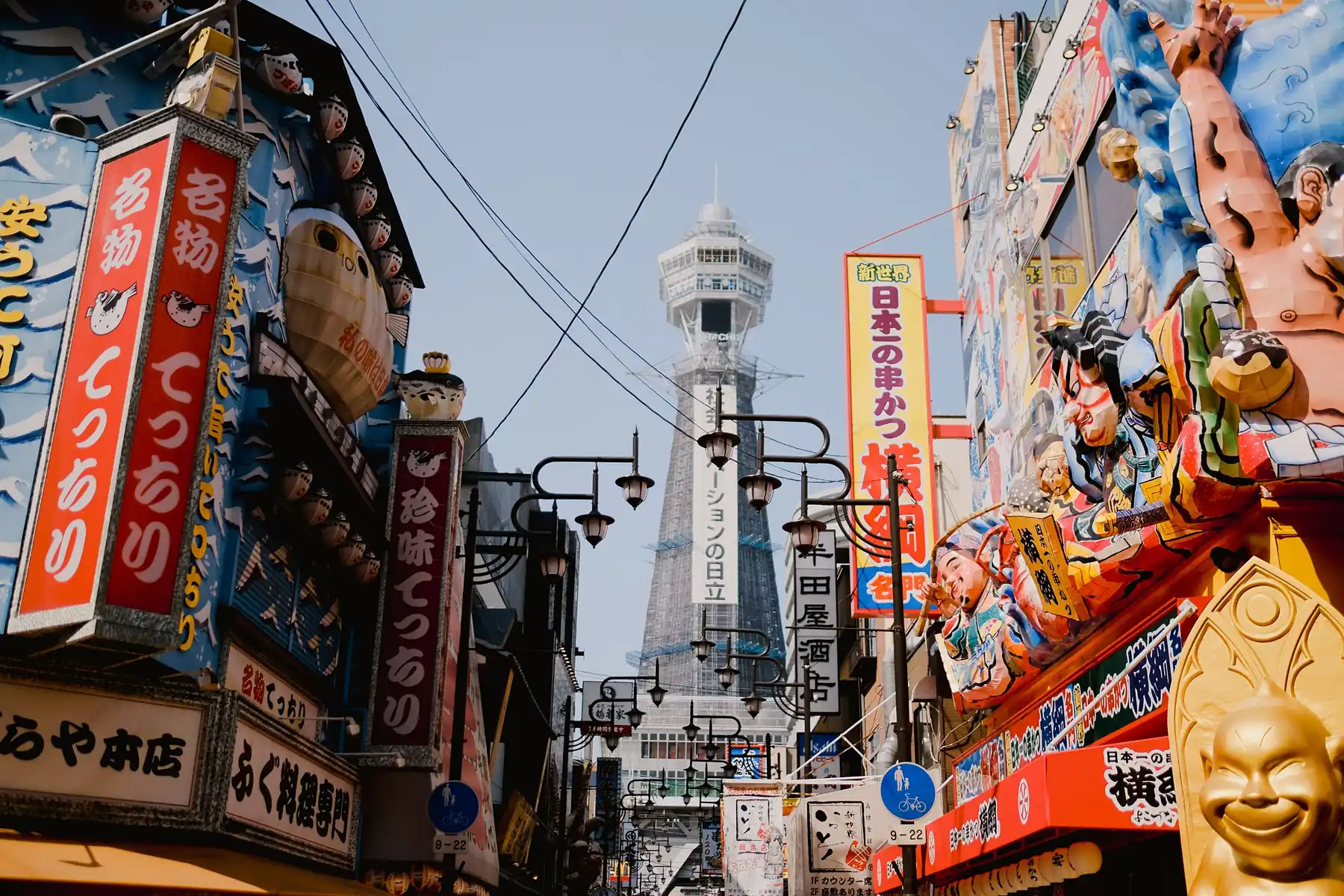 Calle de Osaka llena de carteles de colores, con una torre al fondo