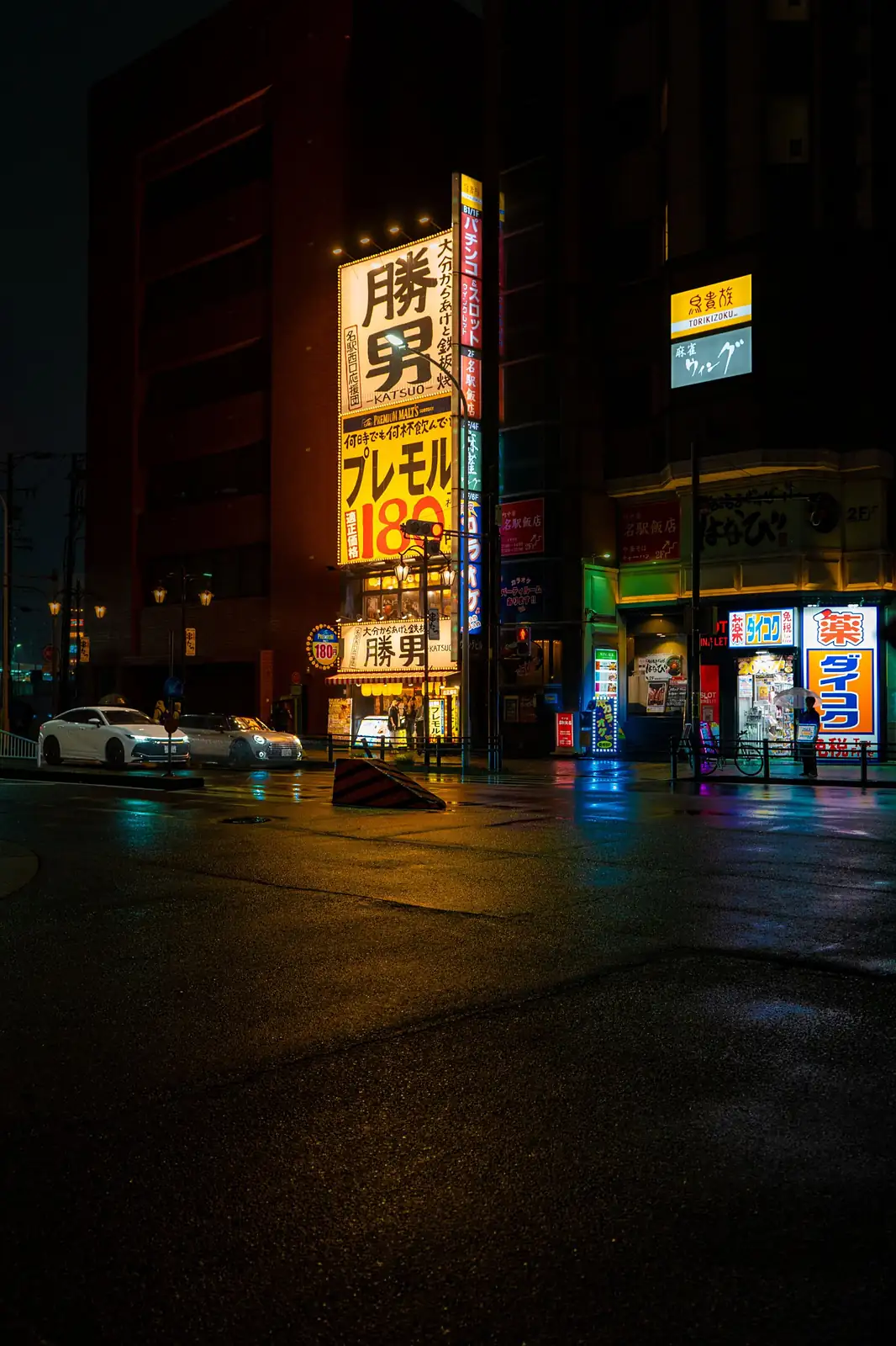 Calle junto a la estación de Nagoya de noche, con letreros luminosos y el suelo mojado por la lluvia
