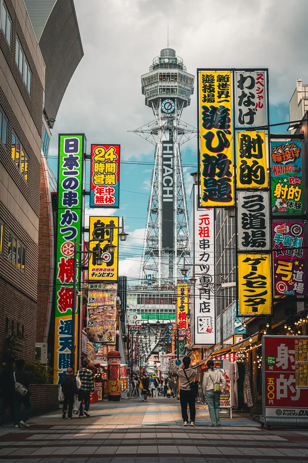 Calle de Osaka llena de grandes letreros de colores, con la torre Tsutenkaku al fondo