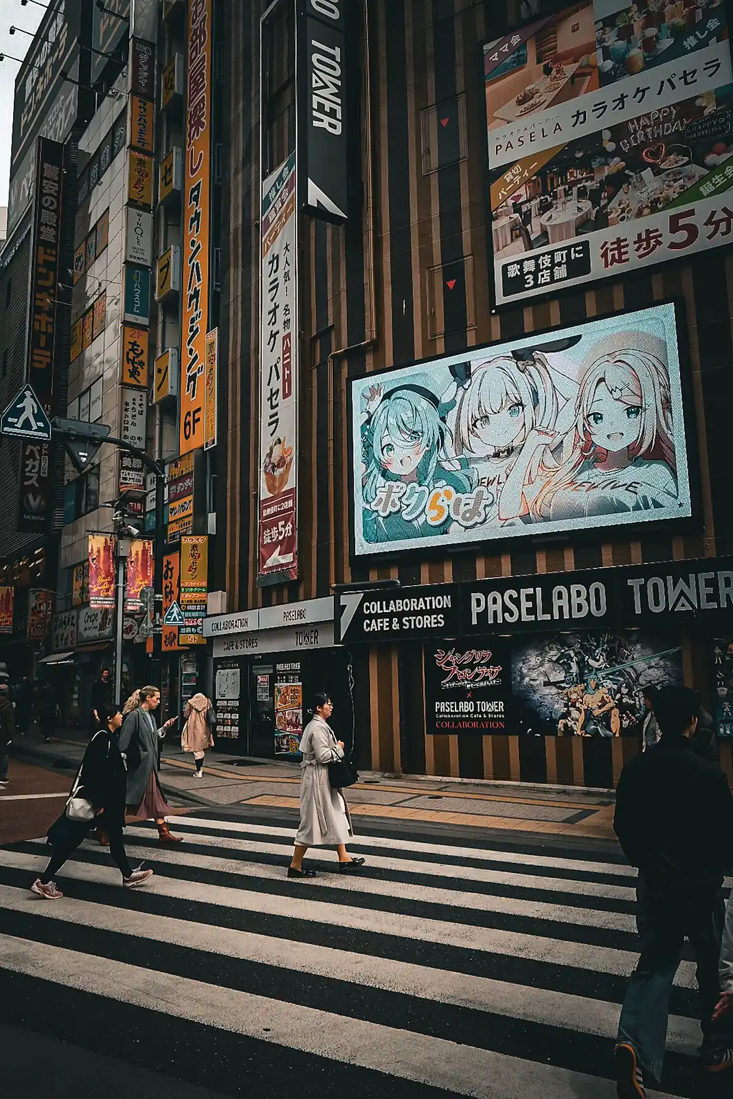 Pantalla con personajes de anime sobre un paso de cebra, junto a un café de colaboración, en Tokio
