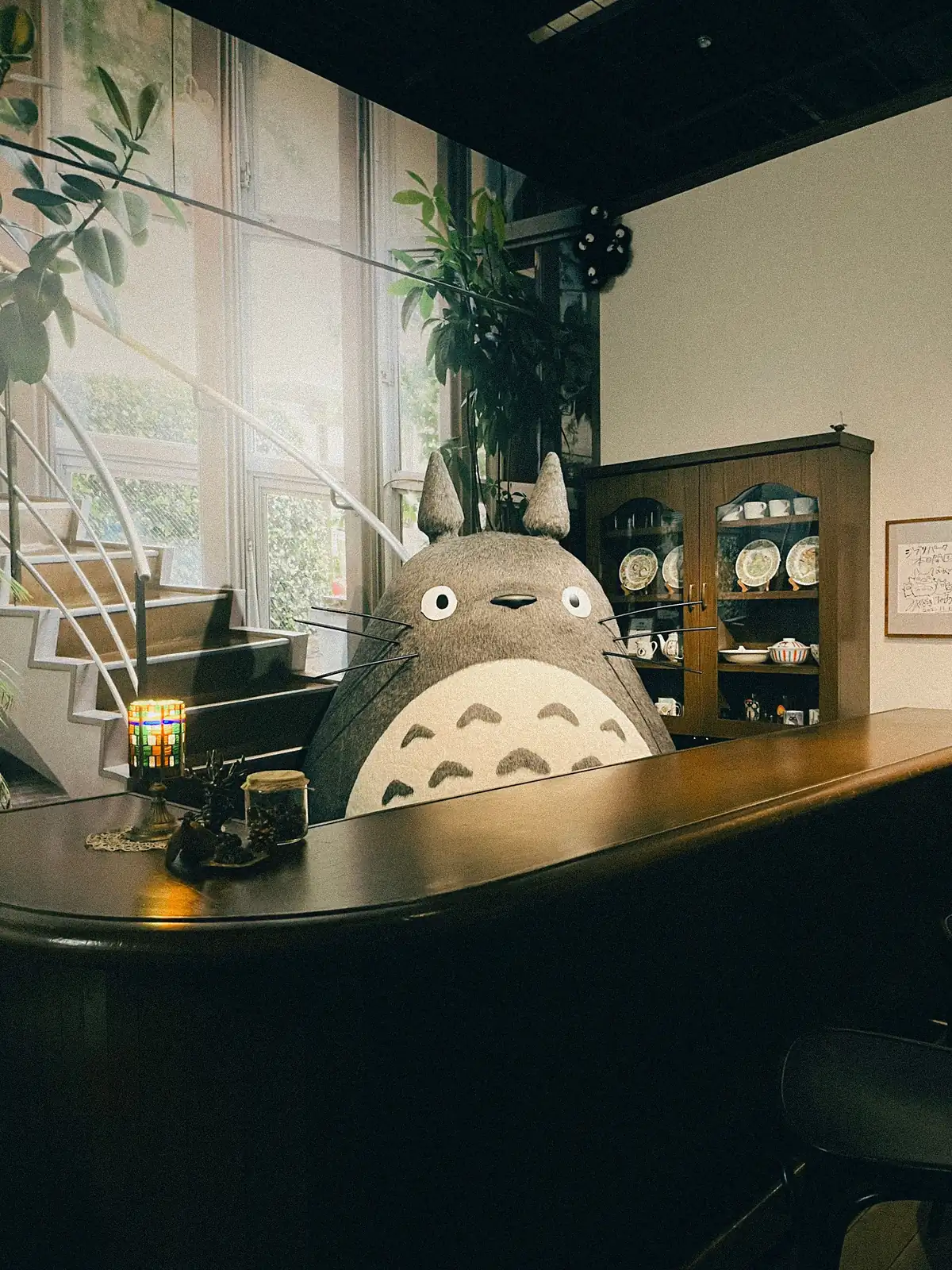 Gran figura de Totoro detrás de una barra de madera, junto a una escalera y una vitrina