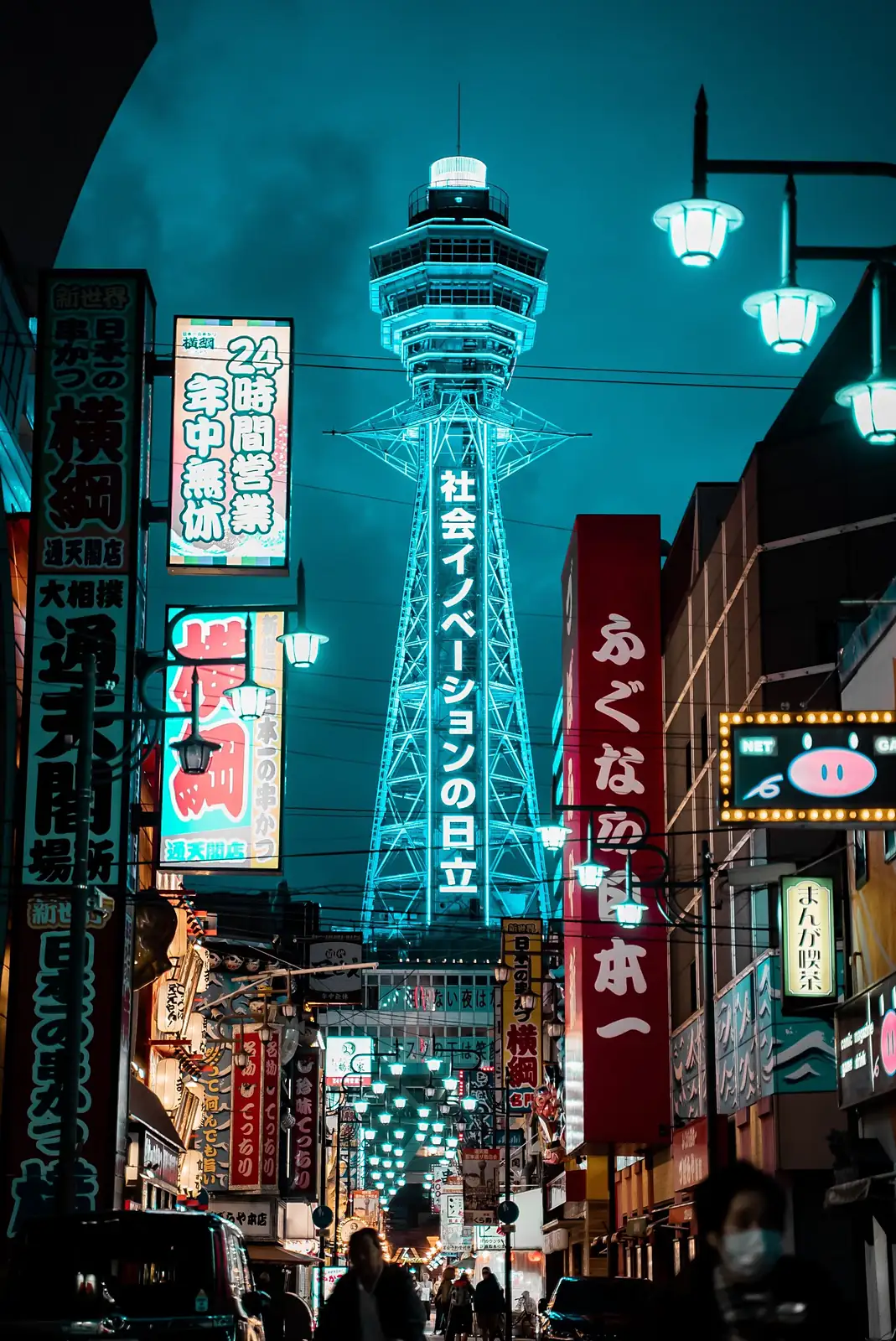 La torre Tsutenkaku iluminada de azul al final de una calle llena de carteles, en Osaka