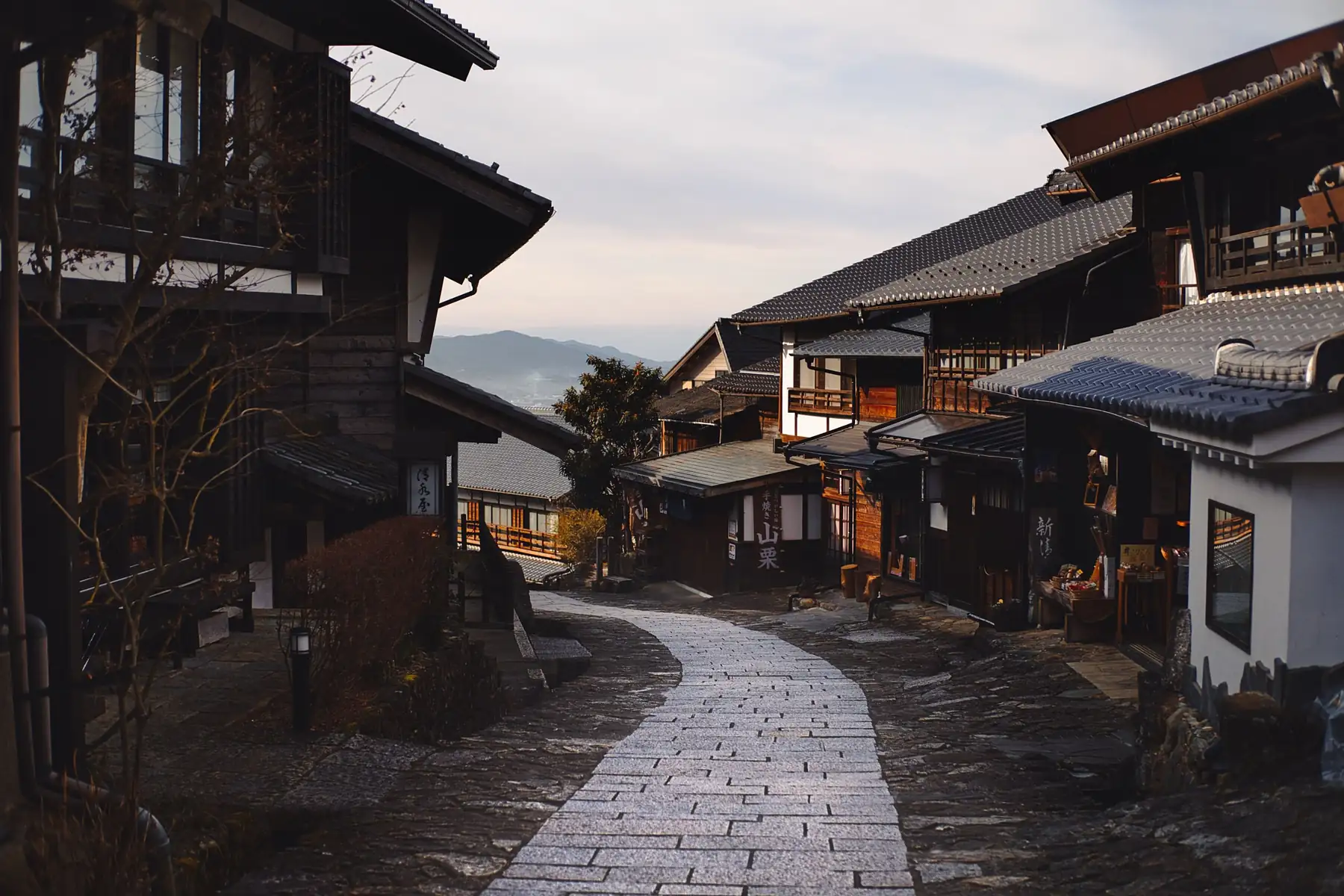 Calle empedrada en cuesta entre casas tradicionales de madera, con montañas al fondo, en Magome, en la ruta Nakasendo