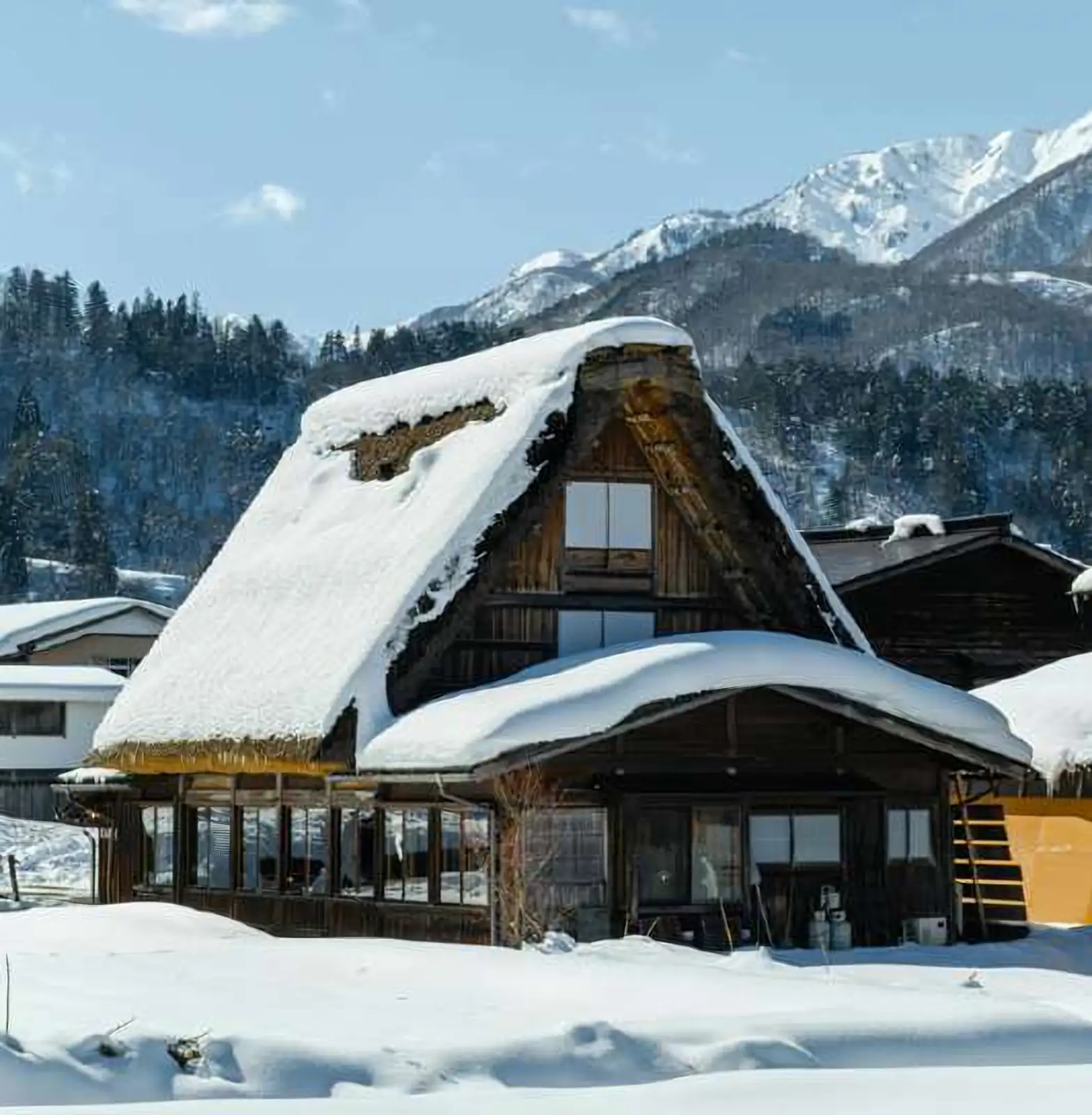 Casa de tejado de paja inclinado cubierta de nieve, con montañas nevadas al fondo, en Shirakawa-go